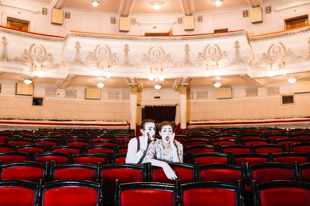 Het mannetje bootst gefluister in geschokt damefoor oorzitting op stoel in auditorium na