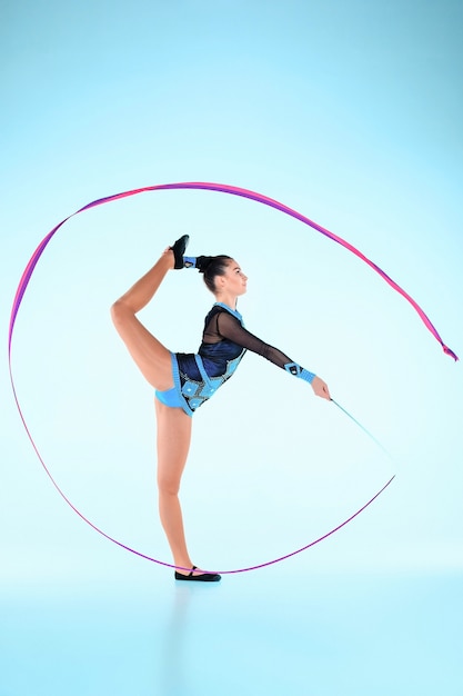 Het meisje dat gymnastiekdans doet met gekleurd lint op een blauwe muur