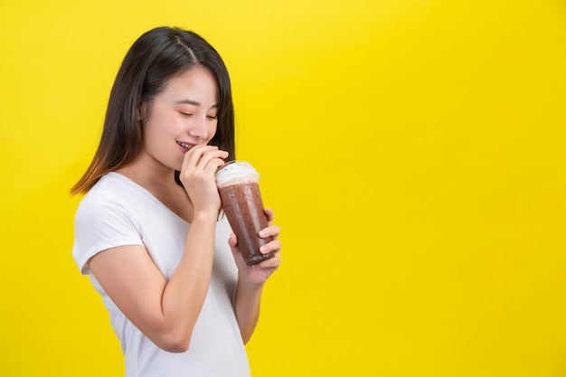 Het meisje drinkt koud water uit cacao uit een doorzichtig plastic glas op een gele.