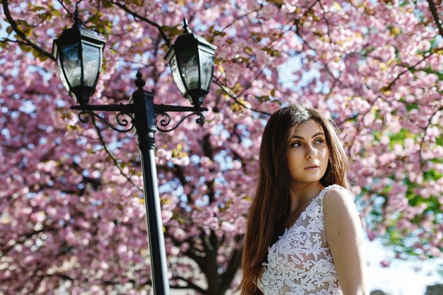 Het meisje in witte kleding bevindt zich onder roze bloeiende sakuraboom in het park