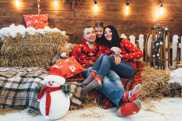 Het meisje kijkt het grappige stellen met haar ouders op het hooi in een Kerstmisstudio