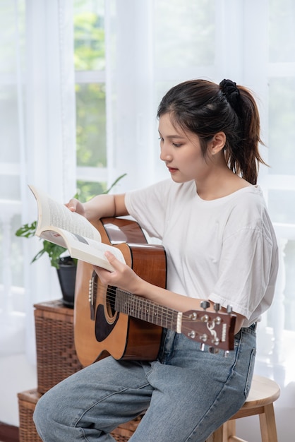 Het meisje zit en speelt gitaar op de stoel.