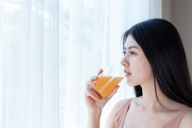 Het mooie Aziatische leuke meisje van de schoonheidsvrouw voelt gelukkig het drinken jus d&#39;orange voor goede gezondheid in de ochtend