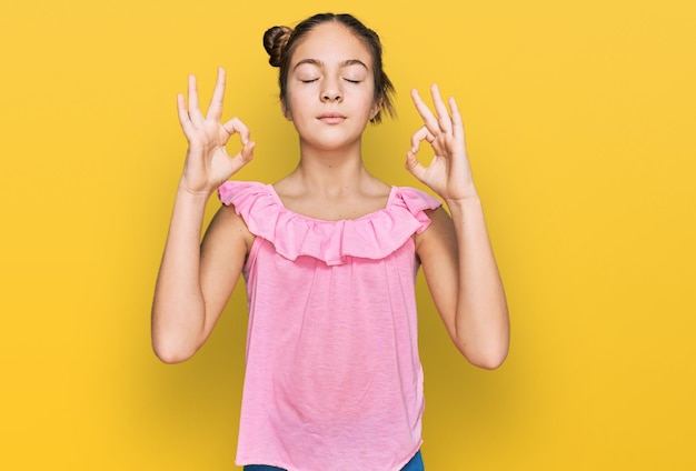 Het mooie donkerbruine meisje die de zomer roze overhemd dragen ontspant en glimlacht met gesloten ogen die meditatiegebaar met vingers doet. yoga-concept.