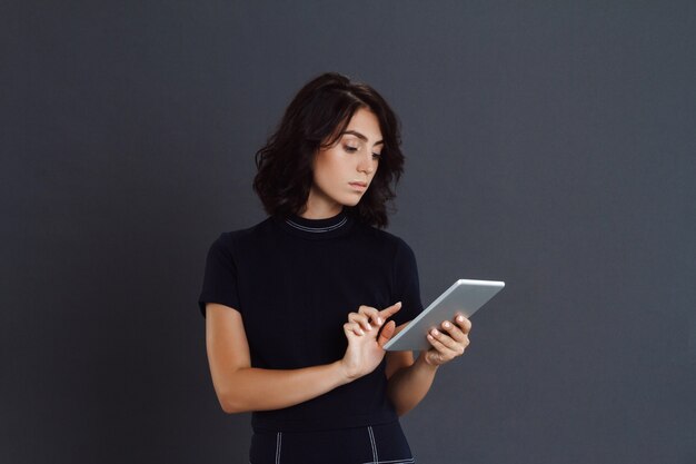 Het mooie jonge vrouw stellen over grijze muur en het houden van tablet in handen