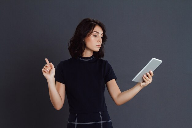 Het mooie jonge vrouw stellen over grijze muur en het houden van tablet in handen