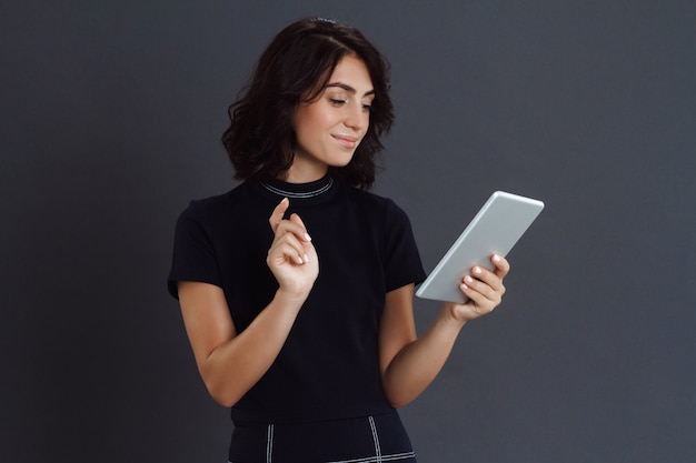 Het mooie jonge vrouw stellen over grijze muur en het houden van tablet in handen