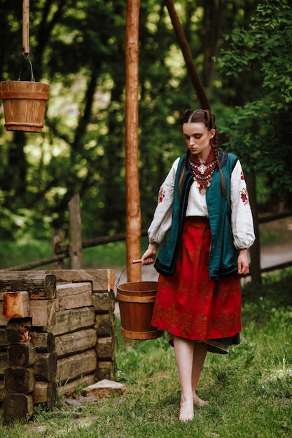 Gratis foto het mooie meisje draagt een wateremmer in een traditionele etnische kleding