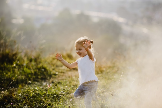 Het mooie meisje in wit overhemd en jeans loopt op het gazon in de mist met groot landschap