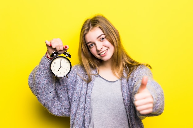 Het mooie meisje van de studententiener met wekker met omhoog geïsoleerde duimen