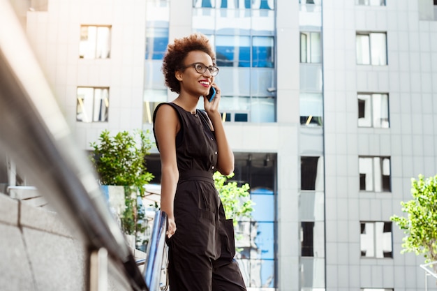 Het mooie vrouw glimlachen die op telefoon spreekt die door stad loopt