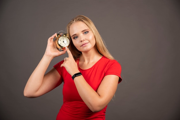 Gratis foto het mooie vrouw stellen met klok op donkere muur.