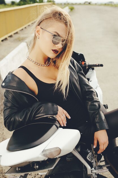 Het mooie vrouw stellen met zonnebril op een motor