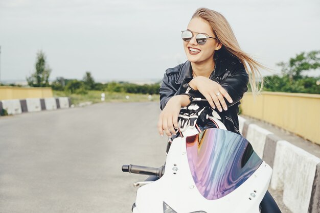 Het mooie vrouw stellen met zonnebril op een motor