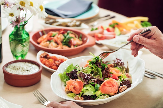 Het nemen van groene salade uit witte kom met vork.