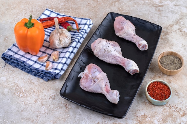Gratis foto het ongekookte vlees van kippenpoten met groenten op een donkere raad