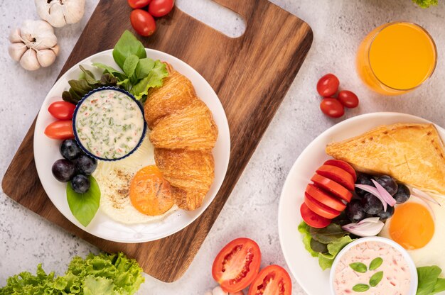 Het ontbijt bestaat uit croissant, gebakken ei, slasaus, zwarte druiven en tomaten.