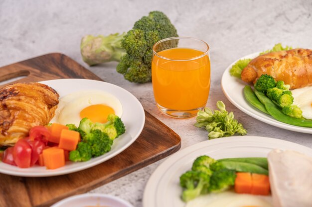 Het ontbijt bestaat uit kip, gebakken eieren, broccoli, wortelen, tomaten en sla op een witte plaat.