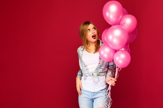 Het opgewekte jonge vrouw stellen met roze luchtballons