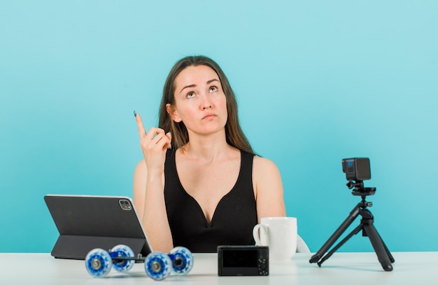 Het opzoeken van blogger meisje wijst omhoog met wijsvinger voor camera op blauwe achtergrond