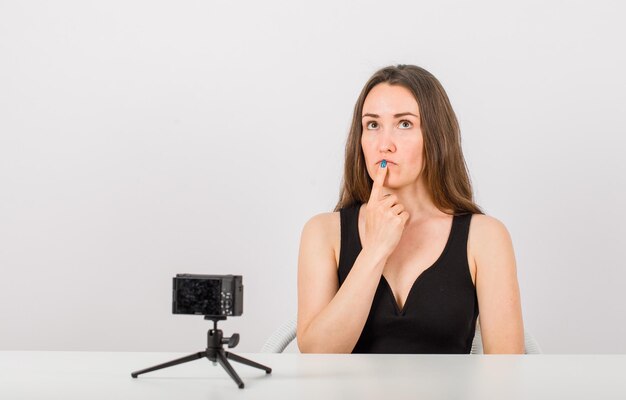 Het opzoeken van een jong meisje denkt door de wijsvinger op de lippen te houden op een witte achtergrond