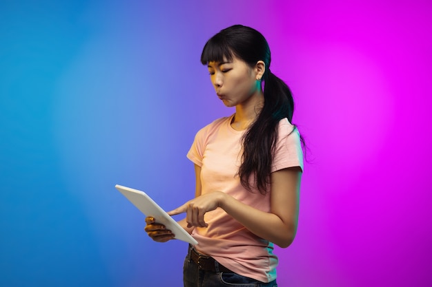 Het portret van de Aziatische jonge vrouw op de achtergrond van de gradiëntstudio in neon. Mooi vrouwelijk model in casual stijl.