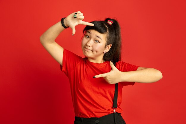 Het portret van de Aziatische tiener dat op rode ruimte wordt geïsoleerd
