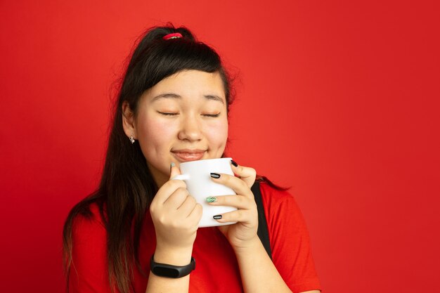 Het portret van de Aziatische tiener dat op rode studio wordt geïsoleerd