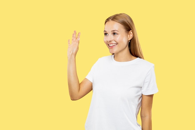 Het portret van de halve lengte van de Kaukasische jonge vrouw op gele studio