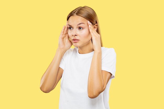 Het portret van de halve lengte van de Kaukasische jonge vrouw op gele studioachtergrond. Mooi vrouwelijk model in wit overhemd