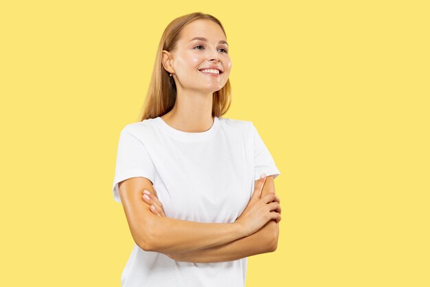 Het portret van de halve lengte van de Kaukasische jonge vrouw op gele studioachtergrond. Mooi vrouwelijk model in wit overhemd