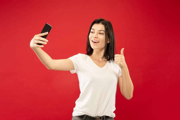 Het portret van de halve lengte van de Kaukasische jonge vrouw op rode studio