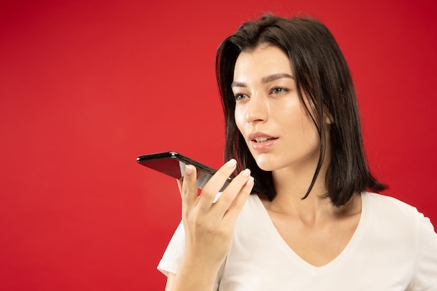 Het portret van de halve lengte van de Kaukasische jonge vrouw op rode studio