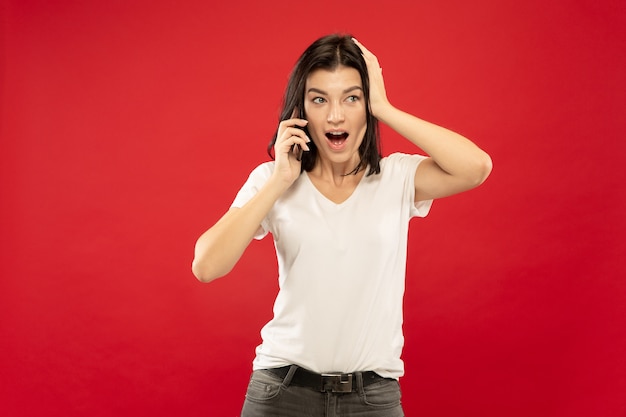 Het portret van de halve lengte van de Kaukasische jonge vrouw op rode studio