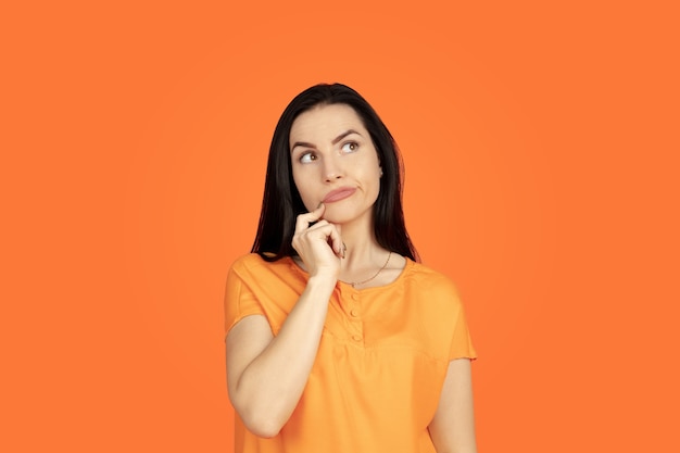 Het portret van de Kaukasische jonge vrouw op oranje ruimte. Mooi vrouwelijk donkerbruin model in overhemd