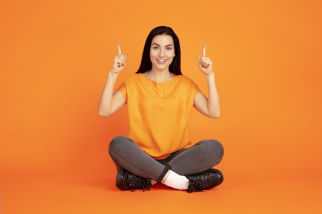 Het portret van de Kaukasische jonge vrouw op oranje ruimte. Mooi vrouwelijk donkerbruin model in overhemd