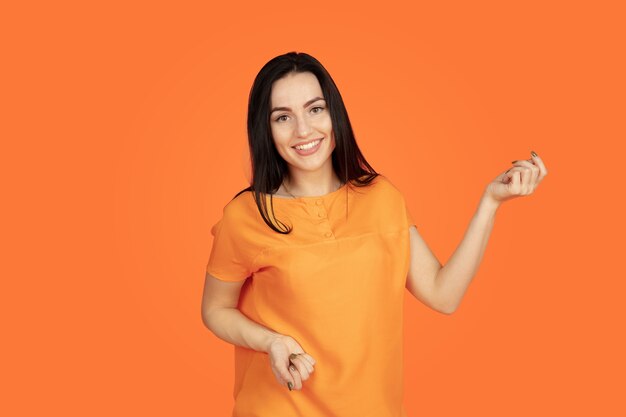 Het portret van de Kaukasische jonge vrouw op oranje studioachtergrond.