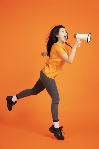 Het portret van de Kaukasische jonge vrouw op oranje studioachtergrond.