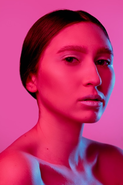 Het portret van de knappe die vrouw op roze studioachtergrond in zwart-wit neonlicht wordt geïsoleerd. Mooi vrouwelijk model. Concept van menselijke emoties, gezichtsuitdrukking, verkoop, advertentie, mode en schoonheid.