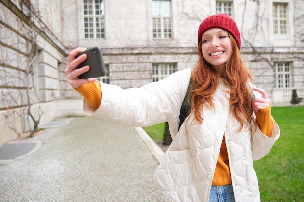 Het portret van een gelukkige meisjestoerist neemt een selfie op een smartphone voor een historisch gebouw dat poseert voor