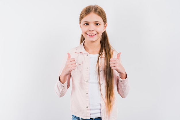 Het portret van een glimlachend meisje die die duim tonen ondertekent omhoog op witte achtergrond wordt geïsoleerd
