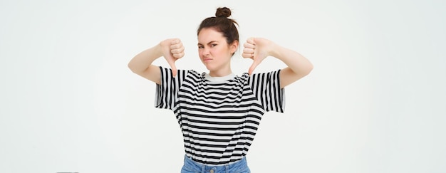 Gratis foto het portret van een teleurgestelde jonge moderne studente toont duimen naar beneden, houdt niet van iets dat ze afkeurt