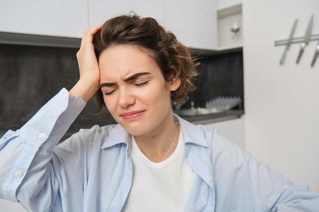 Het portret van een vrouw met een mgiraine-meisje trekt een grimas van pijnlijke hoofdpijn en raakt haar hoofd fronsend aan