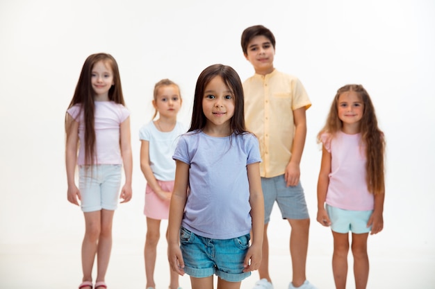 Het portret van gelukkige schattige kleine kinderen jongen en meisjes in stijlvolle vrijetijdskleding camera kijken tegen witte muur