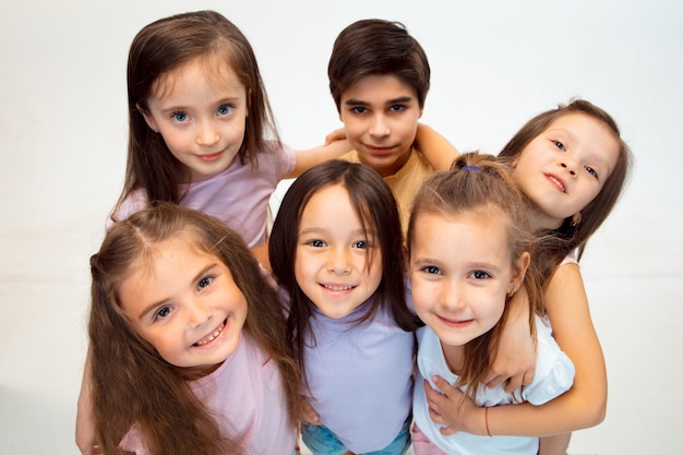 Het portret van gelukkige schattige kleine kinderen jongen en meisjes in stijlvolle vrijetijdskleding voorzijde tegen witte studiomuur kijken