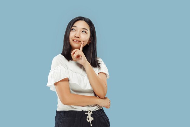 Het portret van halve lengte van de Koreaanse jonge vrouw. Vrouwelijk model in wit overhemd. Denken en glimlachen. Concept van menselijke emoties, gezichtsuitdrukking. Vooraanzicht.