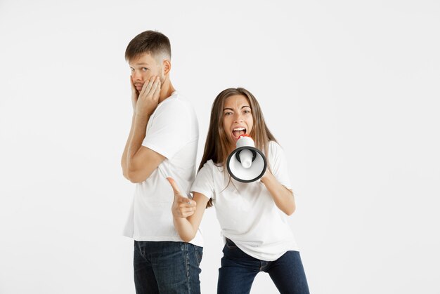 Het portret van het mooie jonge paar dat op witte studioachtergrond wordt geïsoleerd. Gelaatsuitdrukking, menselijke emoties, reclameconcept. Vrouw schreeuwt in mondvrede, gek en gelukkig. De mens is onverschillig.