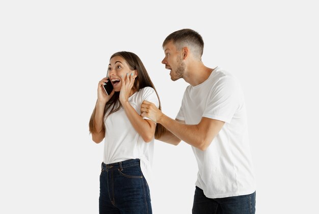 Het portret van het mooie jonge paar geïsoleerd. Gelaatsuitdrukking, menselijke emoties. Vrouw aan de telefoon, man wil haar aandacht op zichzelf schenken.