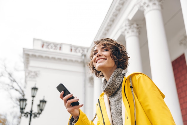 Het portret van inhouds vrouwelijke jaren '20 die modern gadget houden ontvangt tekstbericht op haar smartphone terwijl openlucht het zijn