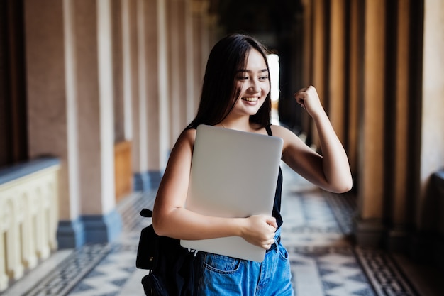 Het portret van jonge Aziatische studente die laptop of een tablet in slim en gelukkig gebruiken stelt aan universiteit of hogeschool,